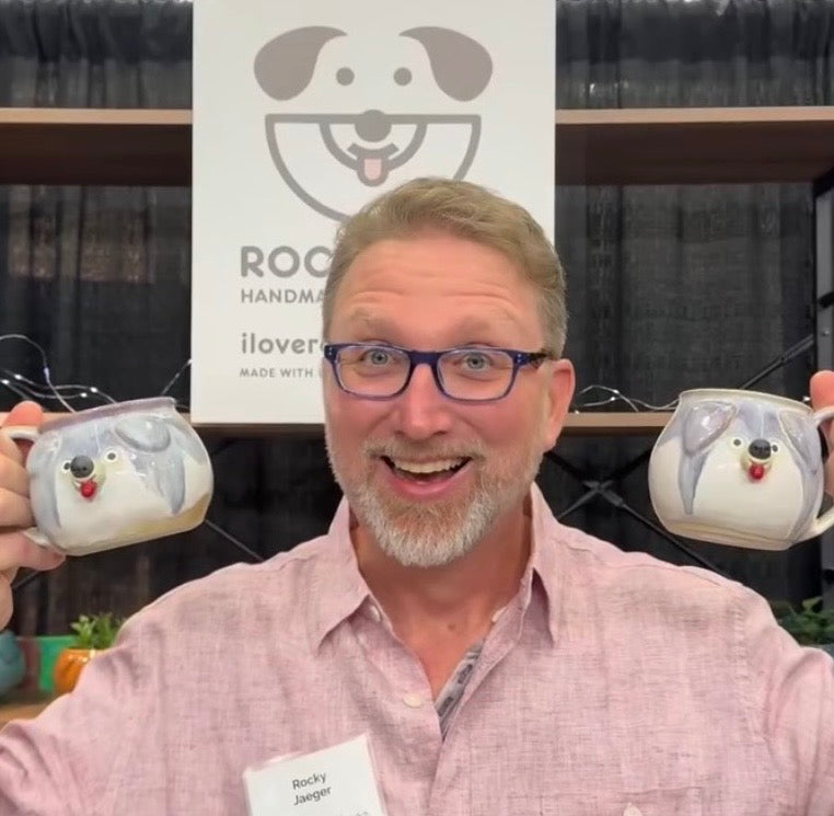 Man holding two ceramic mugs with dog designs in front of a branded backdrop